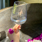 Hand holding the Wine Not? glass over a stone flower bath with pink flowers