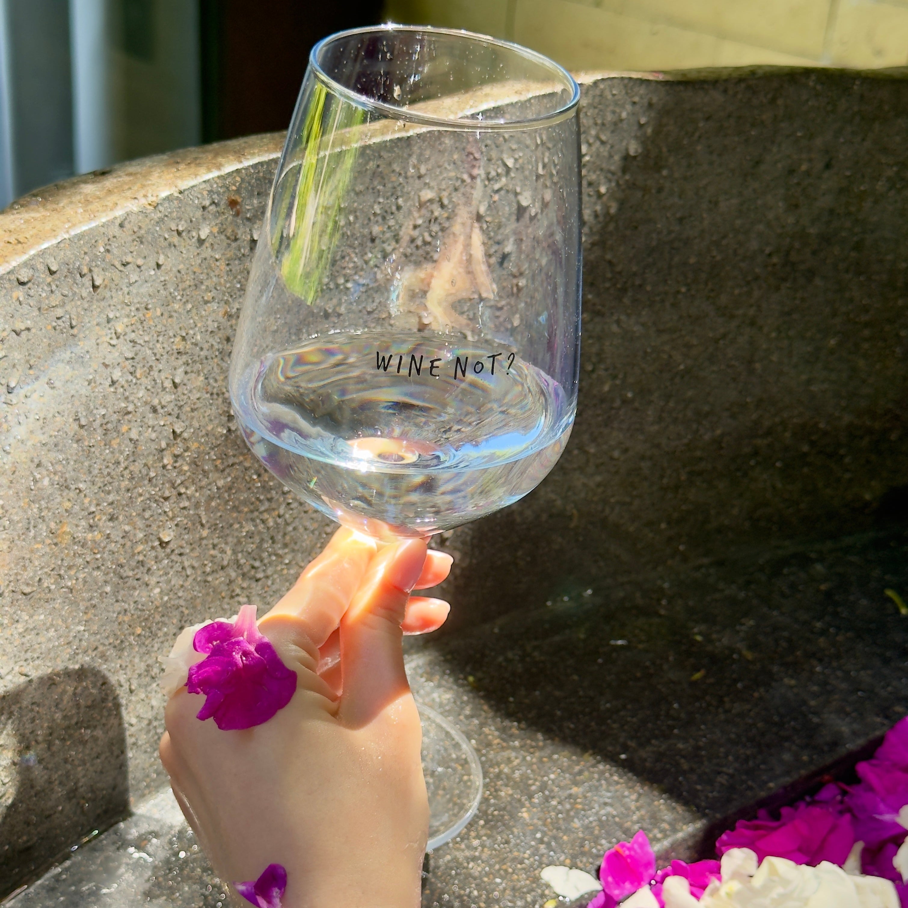 Hand holding the Wine Not? glass over a stone flower bath with pink flowers