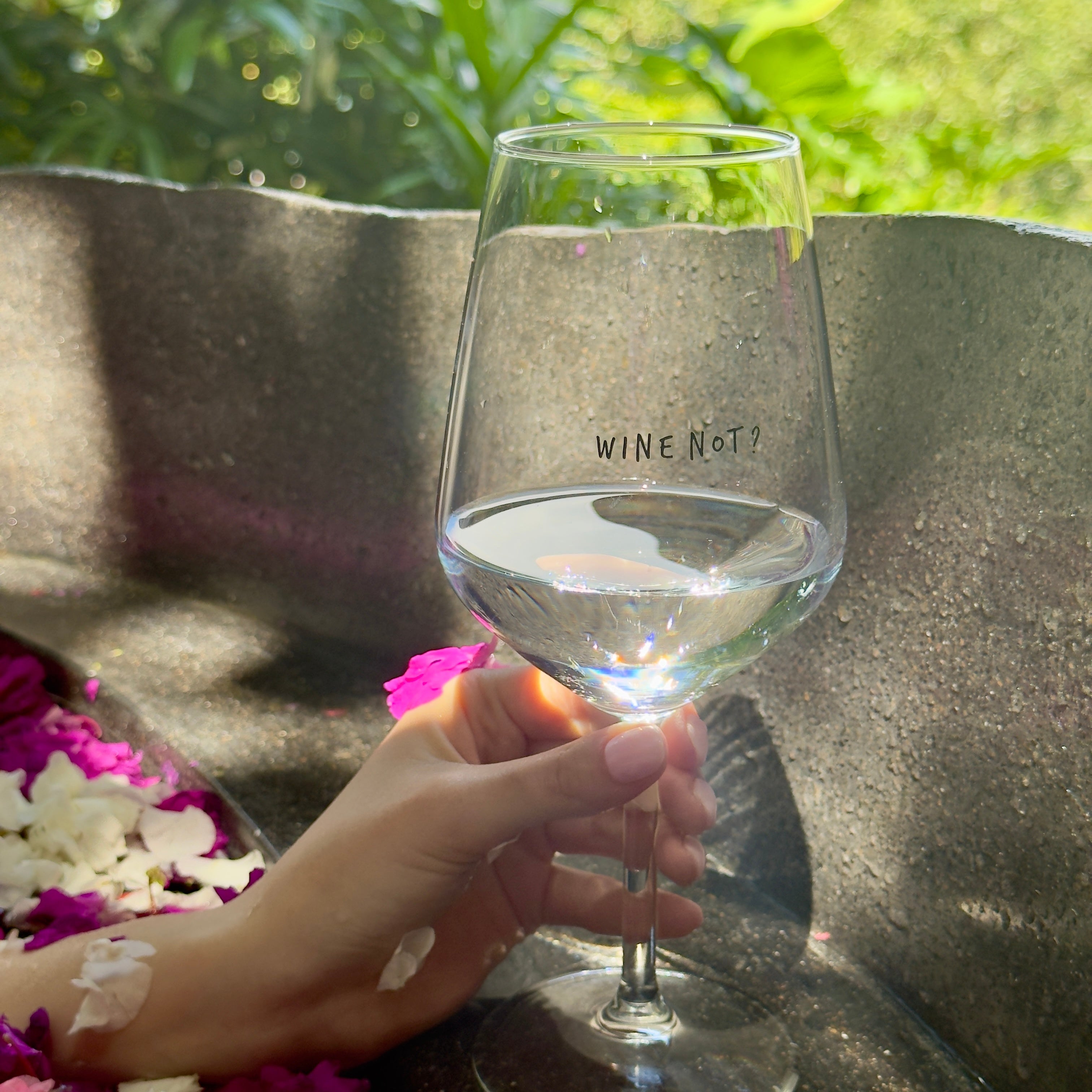 Wine Not? glass filled with white wine, held outdoors among greenery and pink flowers