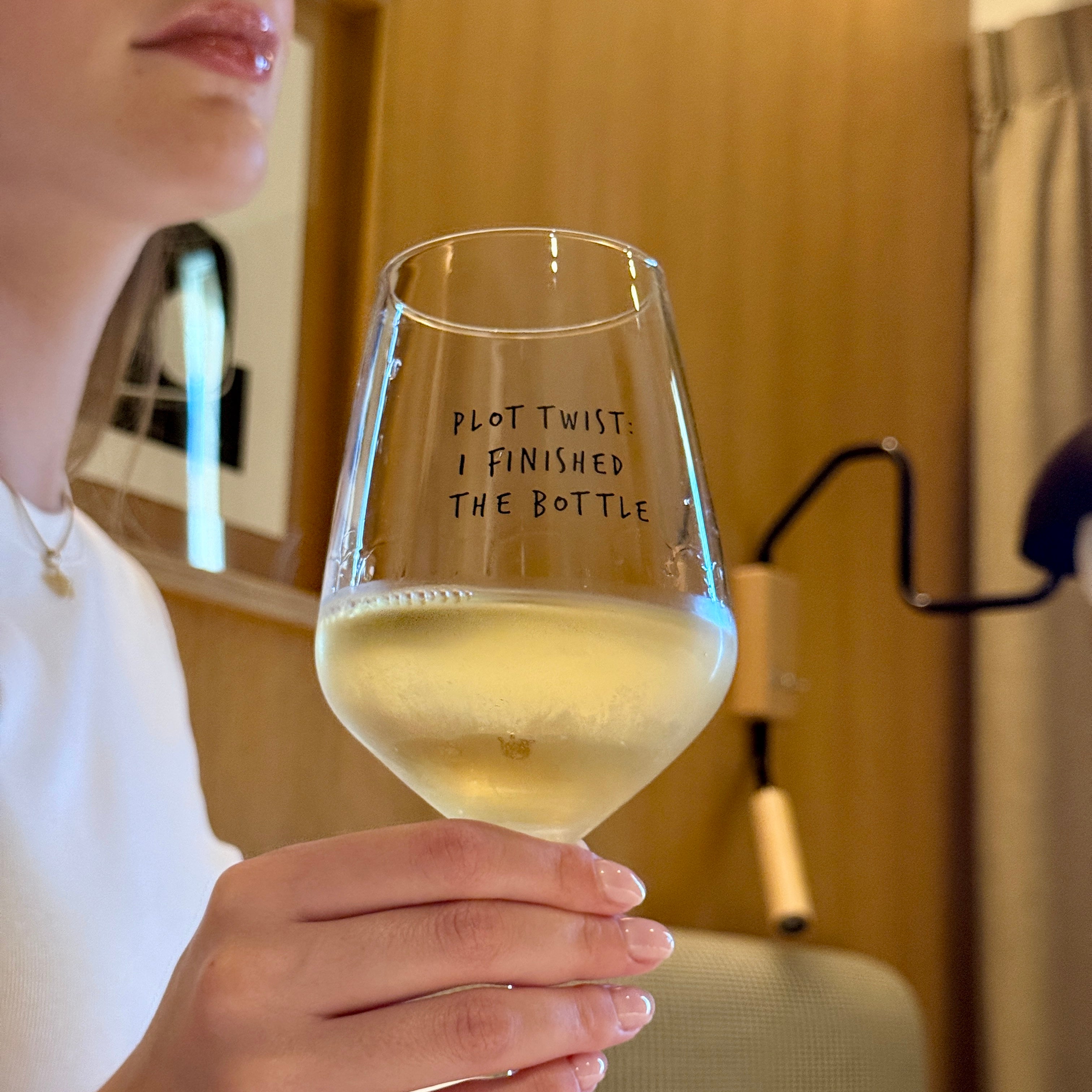 Close-up of a hand holding the Plot Twist glass filled with white wine
