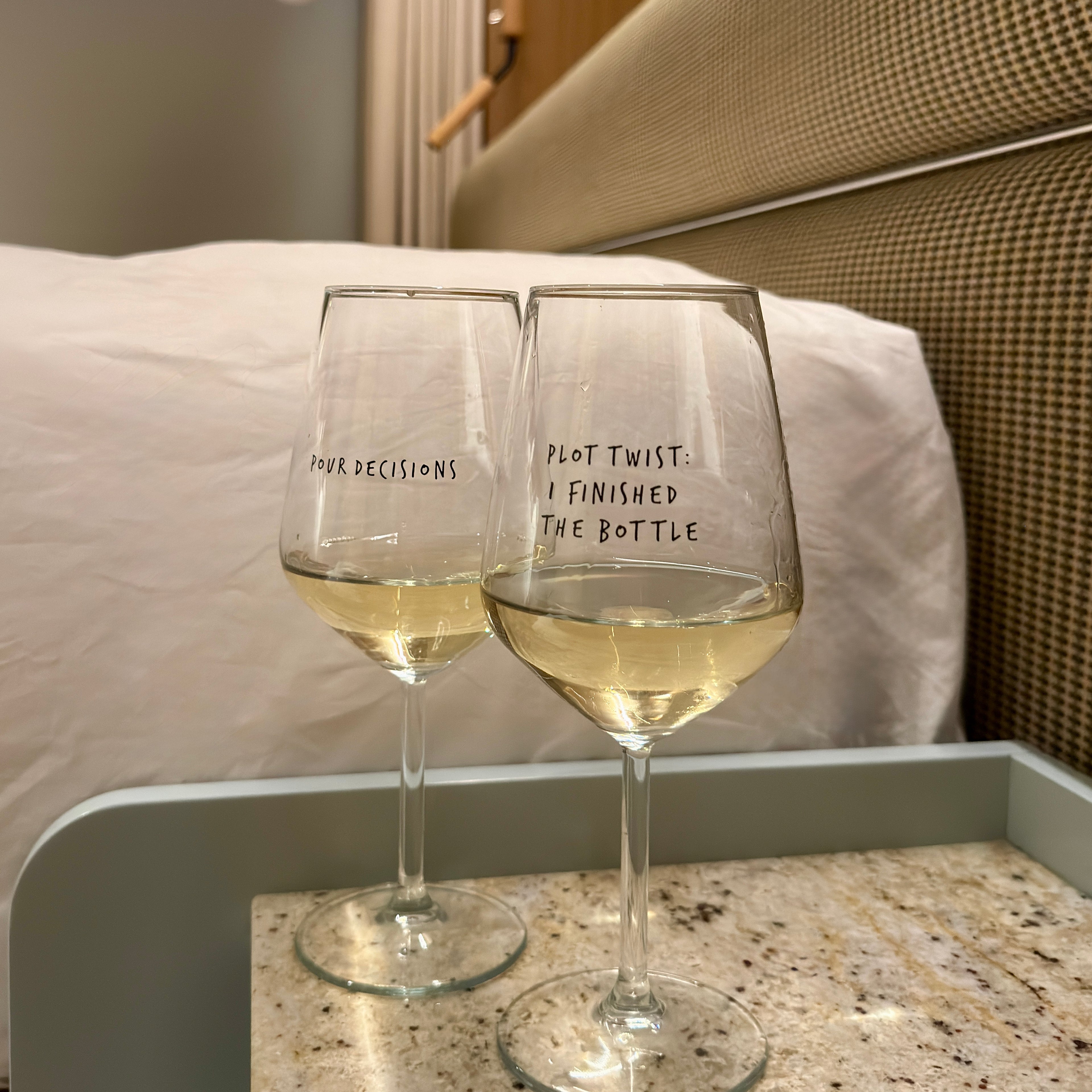 Two wine glasses filled with white wine on a hotel room bedside table. 