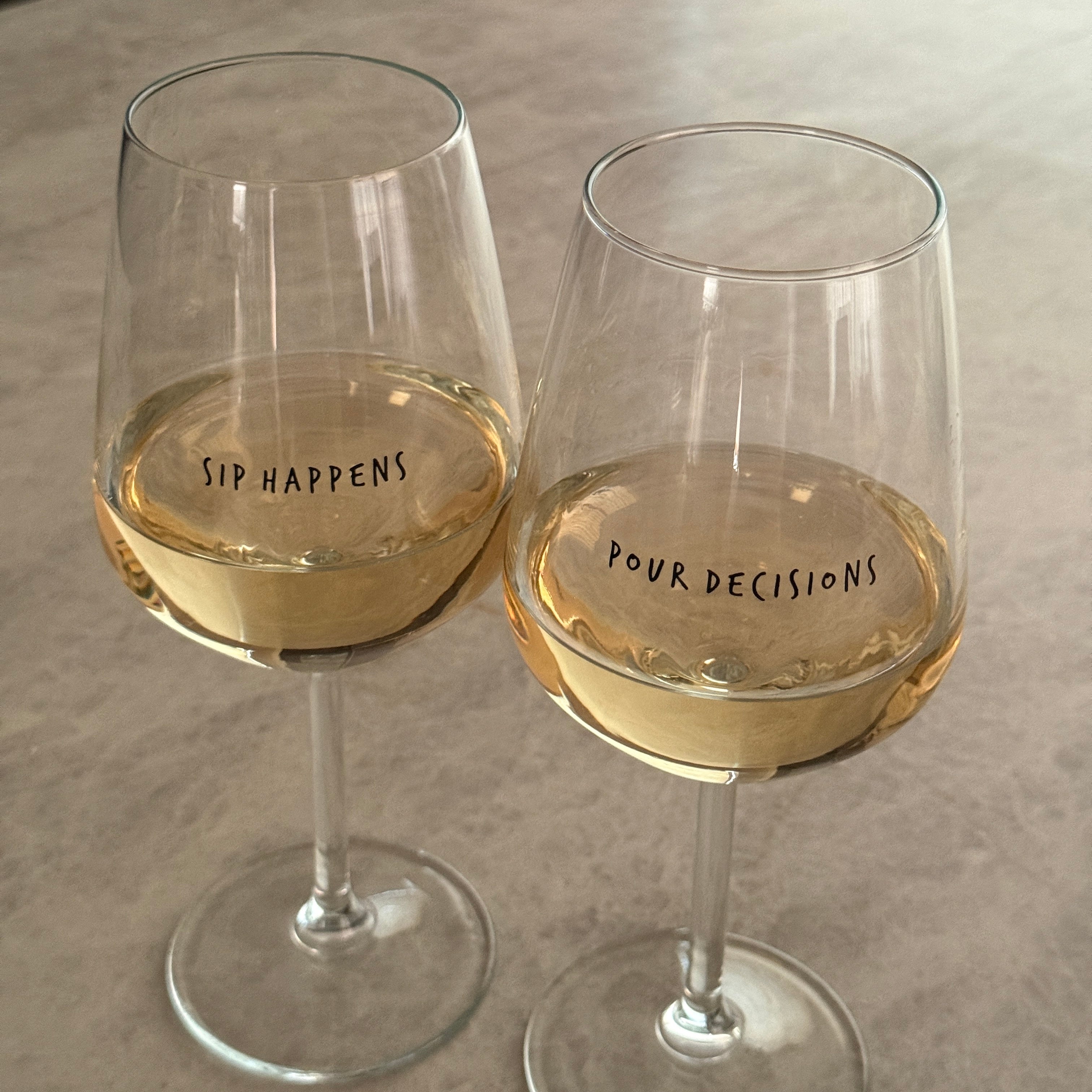 Sip Happens and Pour Decisions wine glasses filled with white wine, side by side